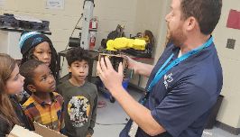  Students watch teacher explain how to operate an handmade robotic arm.
